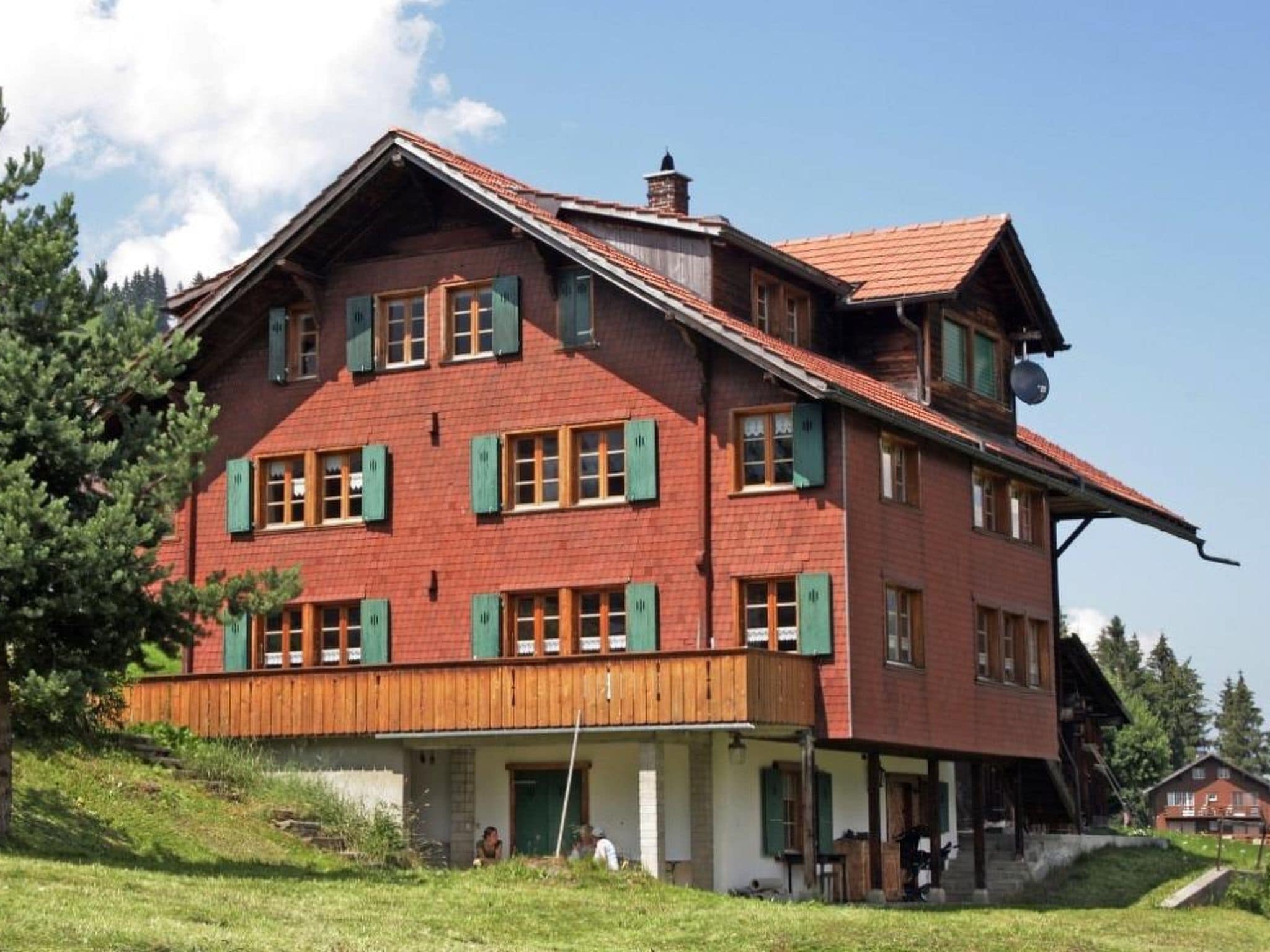 A large, two-story building with a steeply pitched roof, multiple windows with shutters, and a wooden balcony.