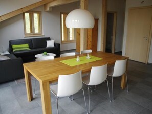 A dining area with a wooden table, four white chairs, and a green placemat. - Anno Domini Appartement/Fewo, Dusche und Bad, WC, 2 Schlafräume 2-Zimmer Studio by Interhome (Adelboden)