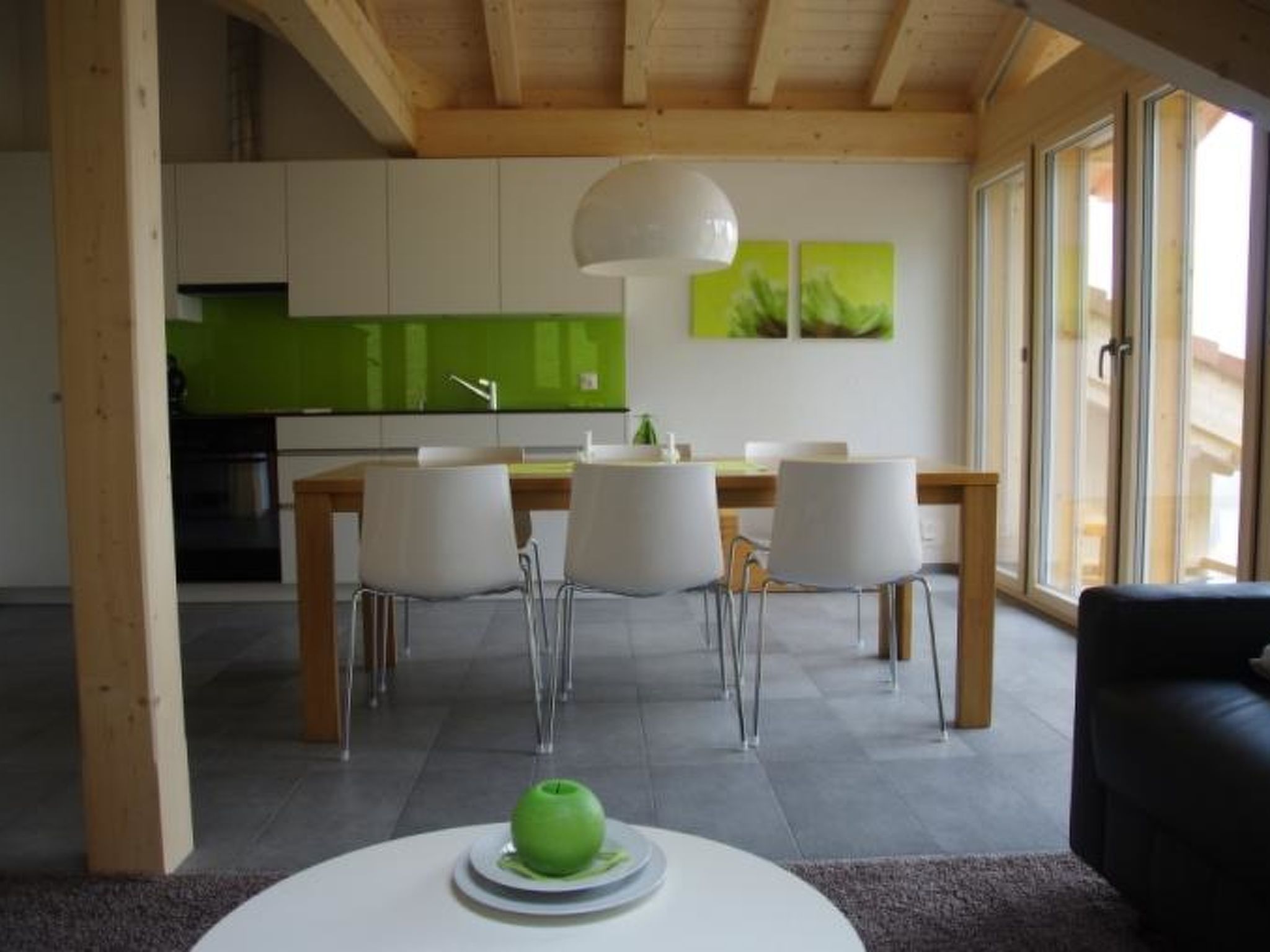 A modern kitchen with green cabinets and a dining area with white chairs and a round table.