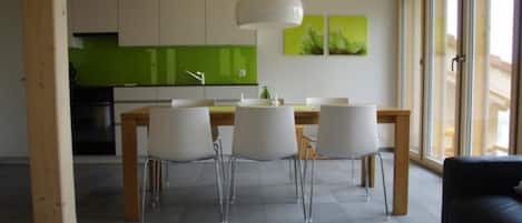 Une cuisine moderne avec des meubles de couleur verte et un coin repas comprenant des chaises blanches et une table ronde.