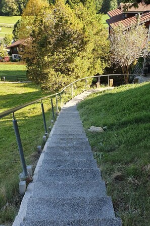 Ein Kiesweg führt zu einem Gebäude mit rotem Dach, umgeben von Grünflächen und Bäumen.