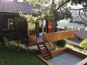 Une maison dotée d’une terrasse en bois, d’un petit espace salon extérieur et offrant une vue sur une vallée.