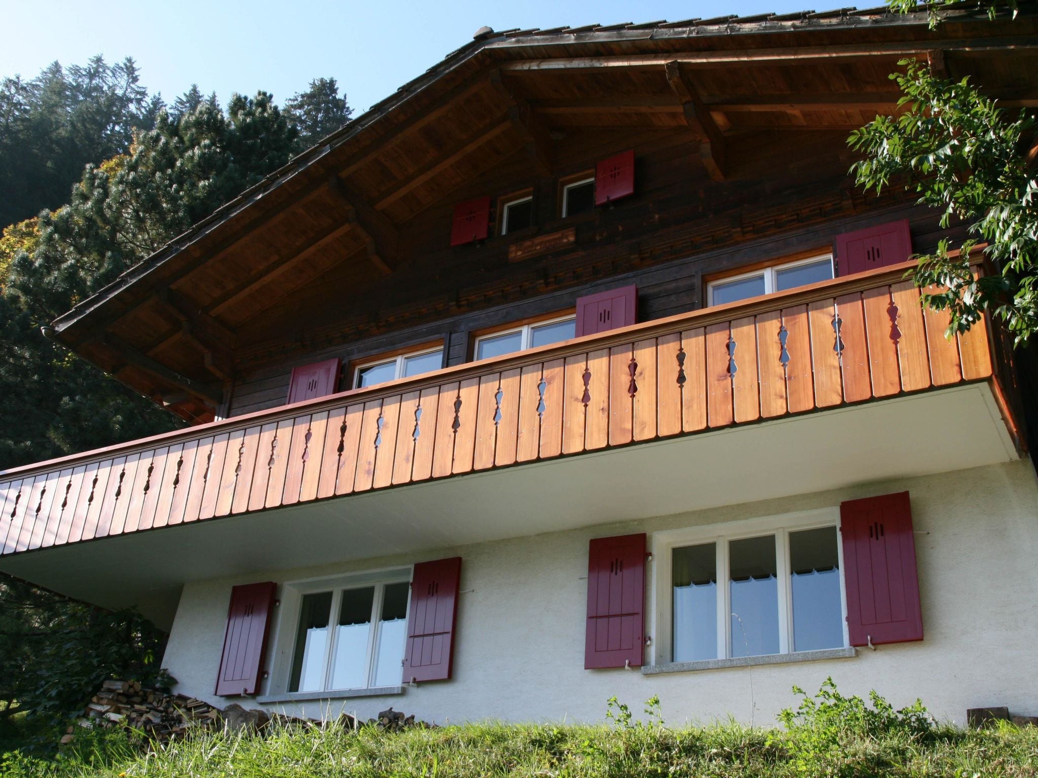 Un bâtiment à deux étages doté d’un balcon, d’une façade en bois et de volets rouges.