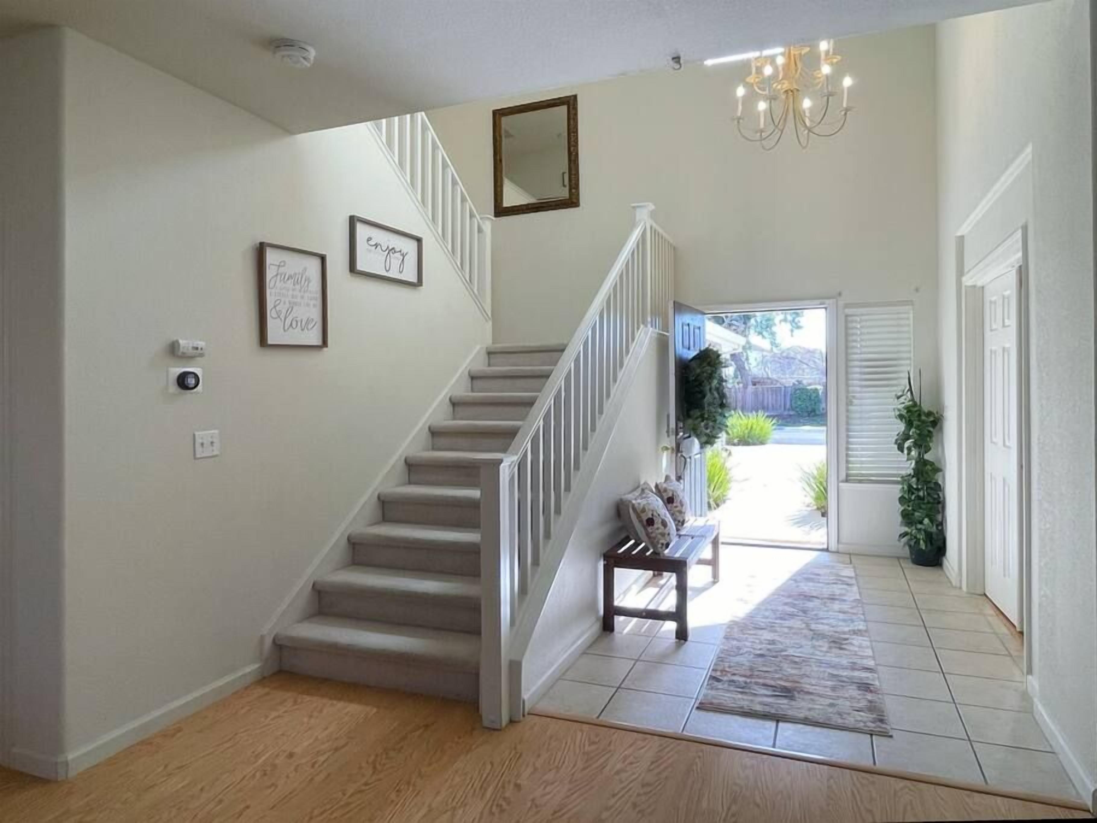 A staircase with a bench, a chandelier, and framed pictures on the wall.
