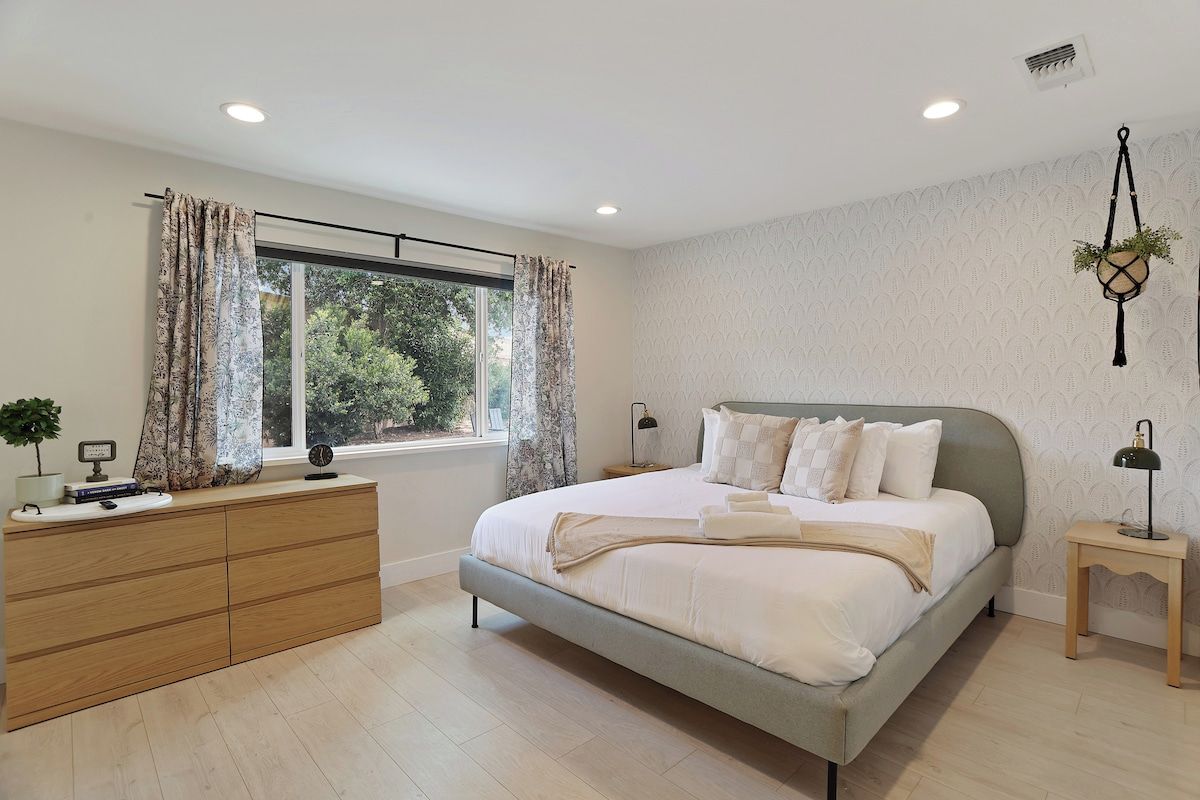A modern bedroom with a bed, bedside tables, a dresser, and a window with curtains.