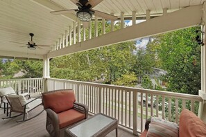 Eine überdachte Veranda mit Korbmöbeln, einem Deckenventilator und Blick auf eine Wohngegend.