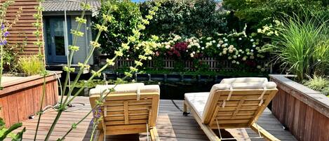 A wooden deck with two lounge chairs and a small garden area with various plants and flowers.