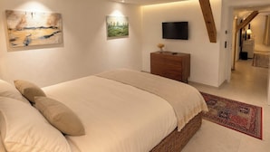 Ein Schlafzimmer mit einem großen Bett, einem Flachbildfernseher, einer Holzkommode und Bildern an den Wänden.