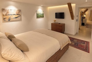 Een slaapkamer met een groot bed, een flatscreen televisie, een houten dressoir en kunstwerken aan de wanden.