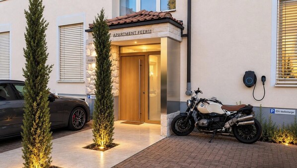 Een gebouw-ingang met een bord waarop 'APARTMENT FEER11' staat, een geparkeerde motor en een auto.