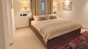 Ein Schlafzimmer mit einem großen Bett, zwei Wandlampen, einem Fenster mit Vorhängen und einem gemusterten Teppich.