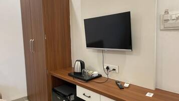 Una habitación con un armario de madera, una televisión de pantalla plana montada en la pared, un refrigerador pequeño, una cafetera y un control remoto sobre la encimera.