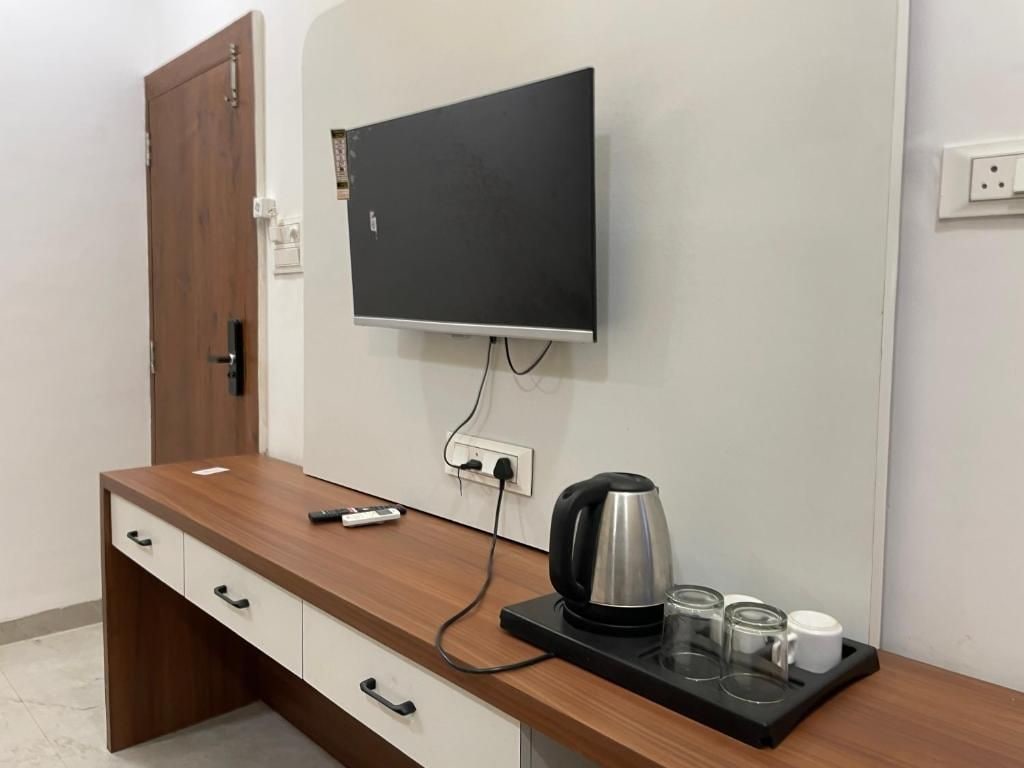 Habitación de hotel con escritorio de madera, televisor de pantalla plana montado en la pared, tetera y bandeja con vasos y una taza.