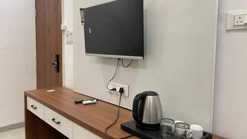 Habitación de hotel con escritorio de madera, televisor de pantalla plana montado en la pared, tetera y bandeja con vasos y una taza.
