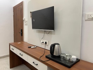 Habitación de hotel con escritorio de madera, televisor de pantalla plana montado en la pared, tetera y bandeja con vasos y una taza.