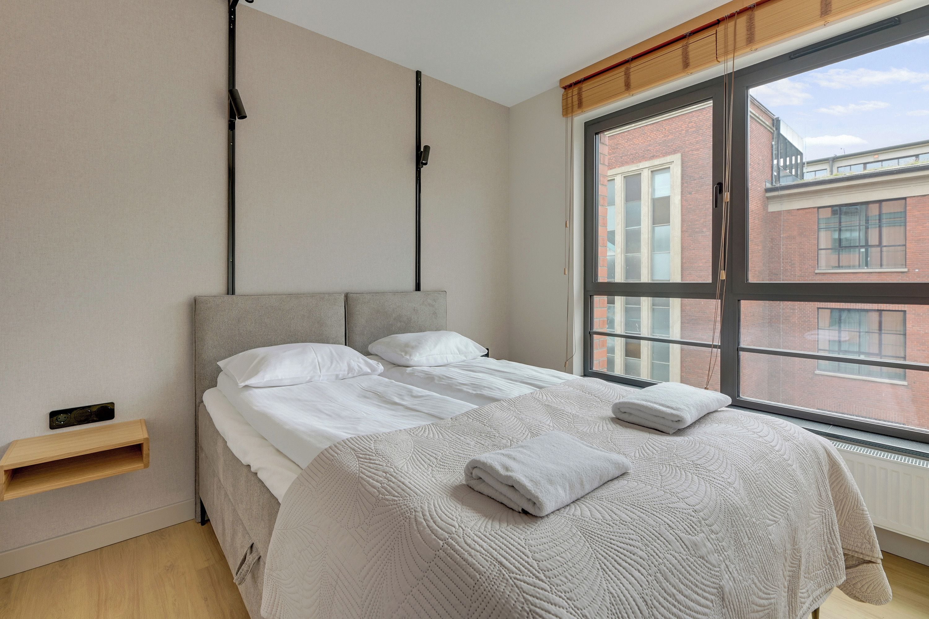 A bedroom with a bed, a window, and a wooden shelf.