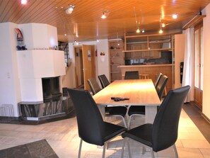 Ein moderner Essbereich mit einem Holztisch und schwarzen Stühlen, einem Kamin und einer Küche im Hintergrund.
