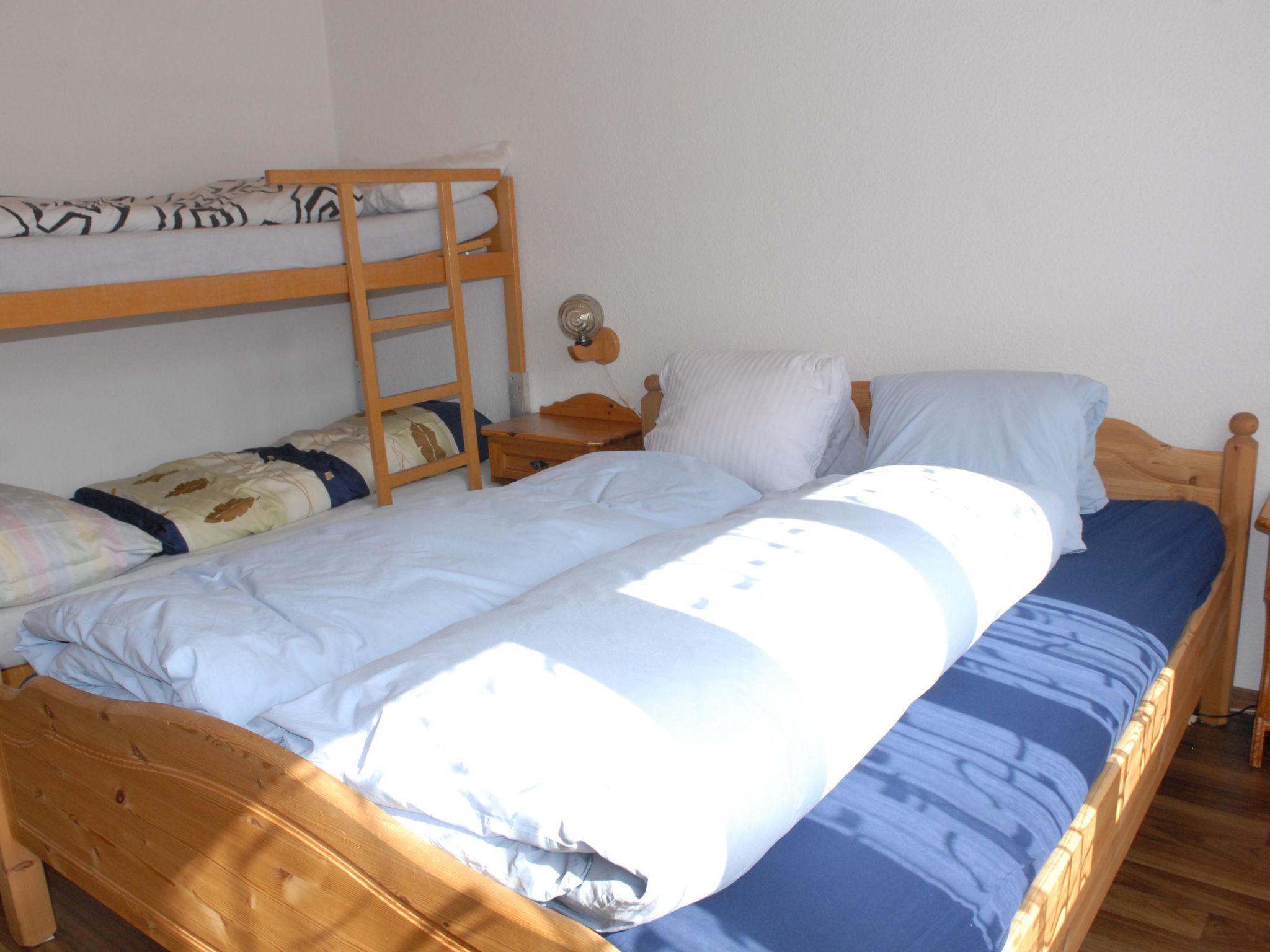 A bunk bed with a lower bunk, a bedside table with a lamp, and a window providing natural light.