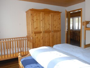 Quarto com guarda-roupa de madeira, berço e cama com roupa de cama branca.