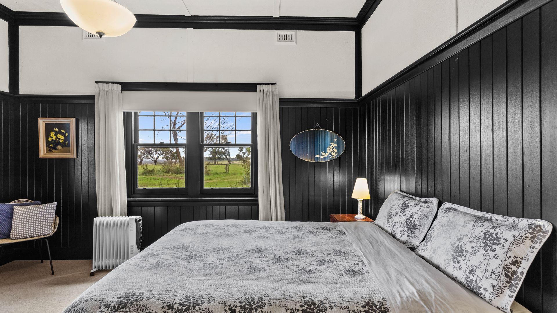 A bedroom with a large bed, a window with a view of the outdoors, a radiator, and a bedside table with a lamp.