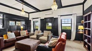 A room with a brown leather sofa, patterned armchairs, a wooden coffee table, and a bookshelf. - Byfrons Phillip Island Road (Cowes)
