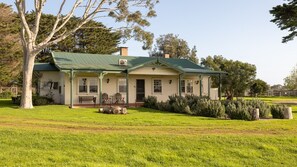 A two-story house with a green roof, a porch with seating, and a well-maintained lawn. - Byfrons Phillip Island Road (Cowes)