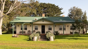 A two-story house with a green roof, a front porch with chairs, and a pathway leading to the door. - Byfrons Phillip Island Road (Cowes)