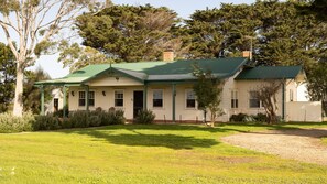 A two-story house with a green roof, surrounded by a well-maintained lawn and various shrubs. - Byfrons Phillip Island Road (Cowes)