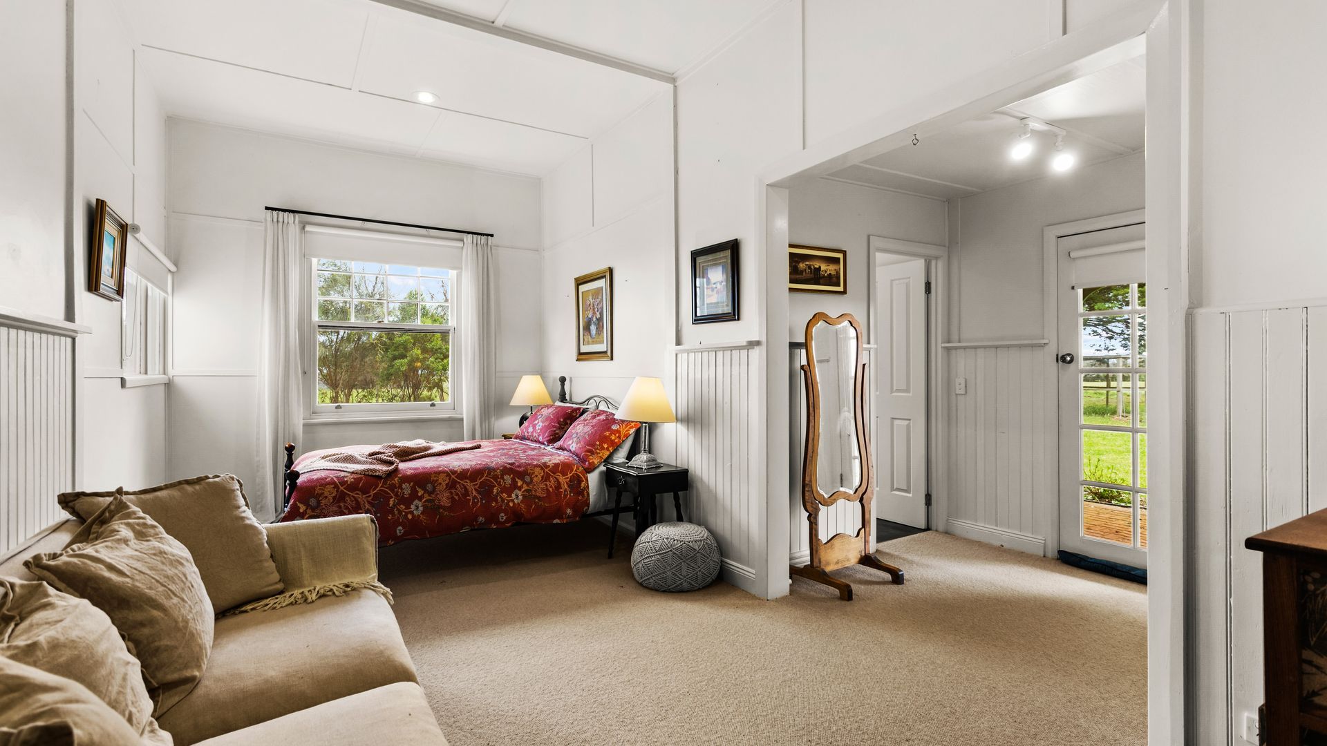 Un dormitorio con cama, lámparas de noche, un espejo y vistas al exterior a través de una puerta.