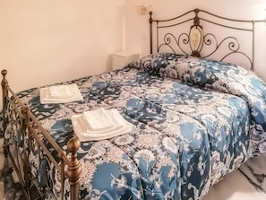 A bed with a floral patterned bedspread, a wooden headboard, and two white towels.