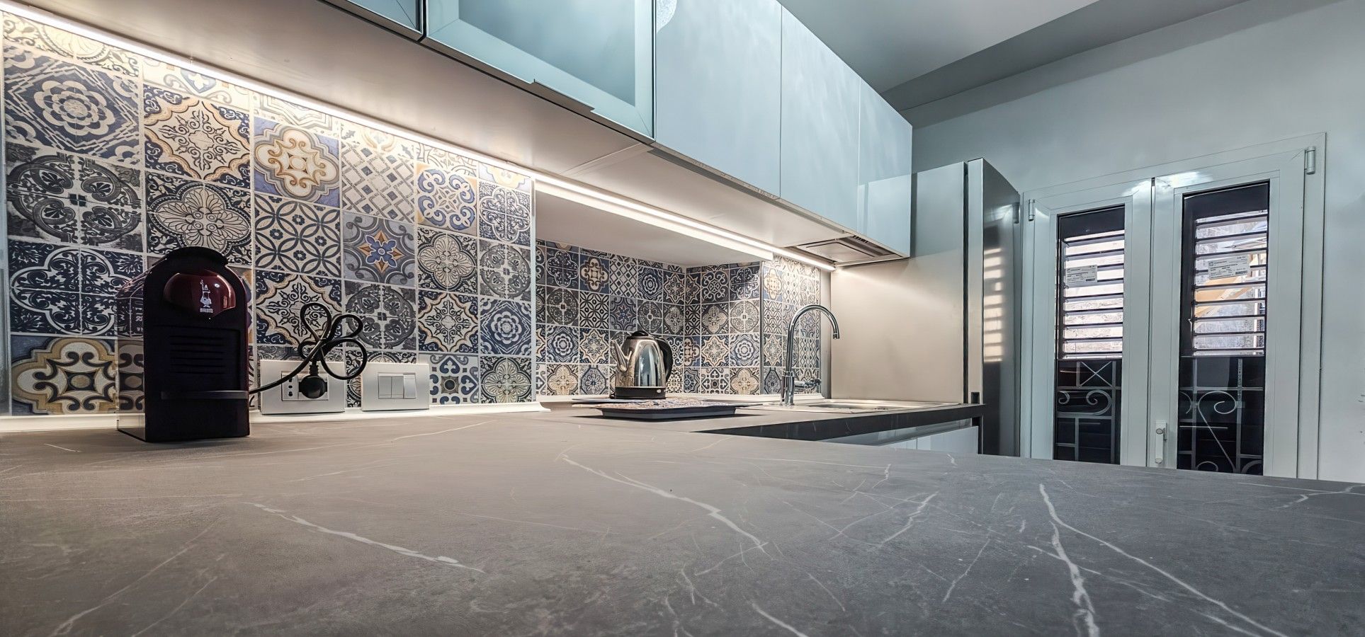 Una cucina moderna con piano di lavoro in marmo, backsplash decorato ed elettrodomestici in acciaio inossidabile.
