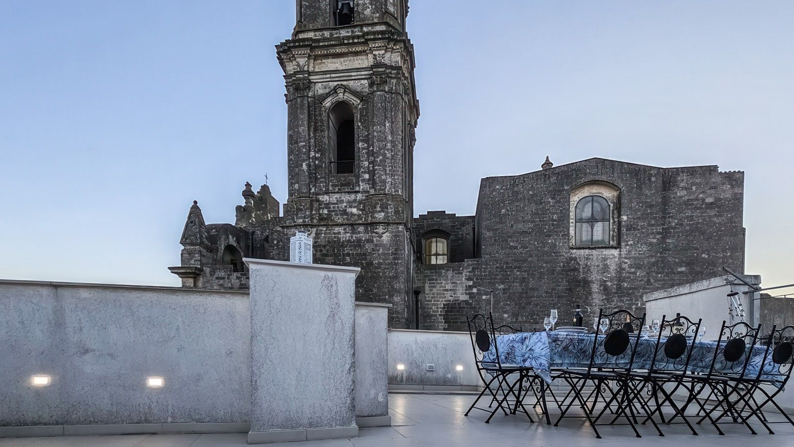 Une terrasse sur le toit, avec une table dressée pour le dîner, d’où l’on peut admirer un ancien bâtiment en pierre doté d’un clocher.