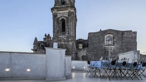 Une terrasse sur le toit, avec une table dressée pour le dîner, d’où l’on peut admirer un ancien bâtiment en pierre doté d’un clocher.
