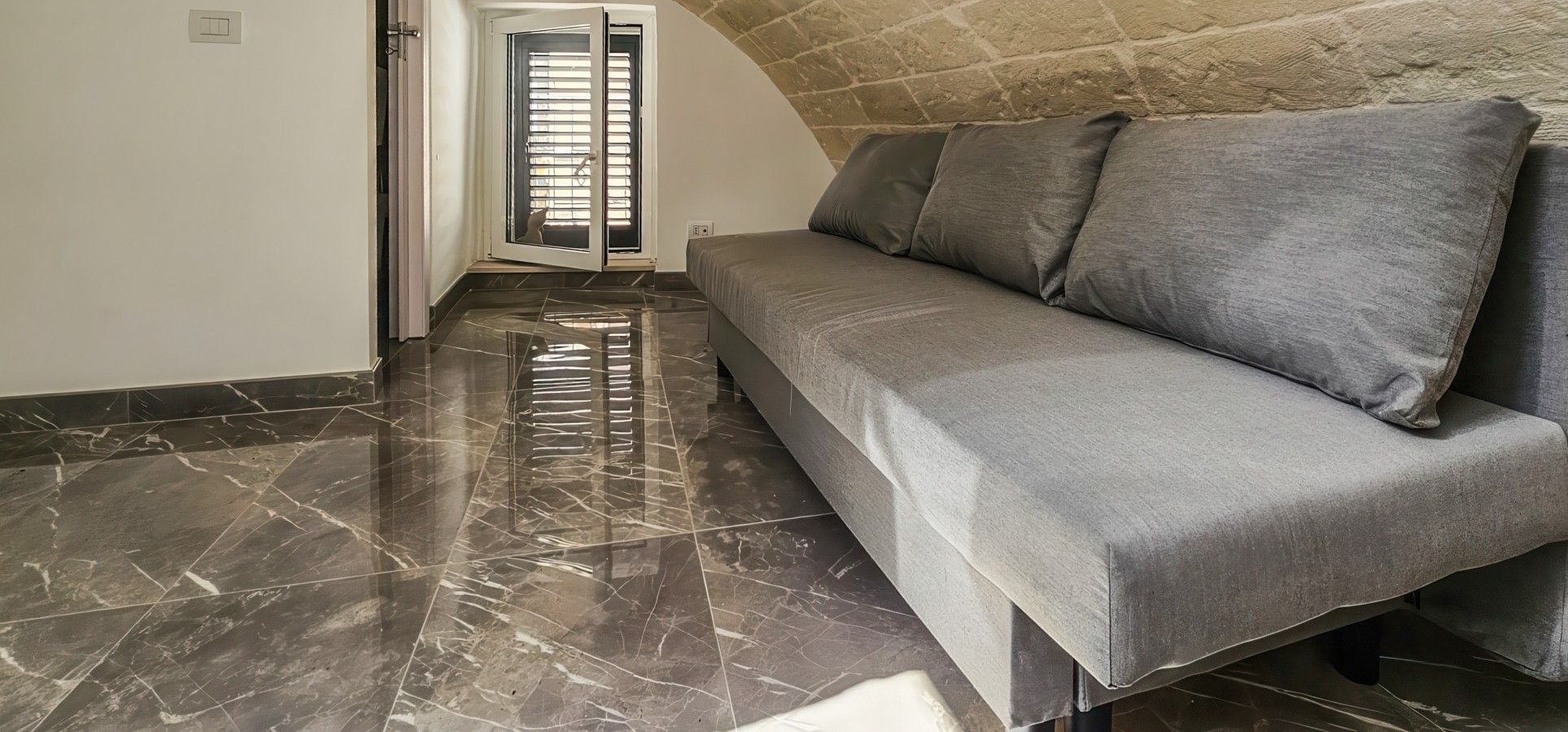 Ein modernes Interieur mit einem grauen Sofa, einem Fliesenboden und einer Steinwand.