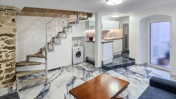 Un intérieur moderne avec un mur en pierre, un escalier, une cuisine et un espace de vie doté d’un sol en marbre.