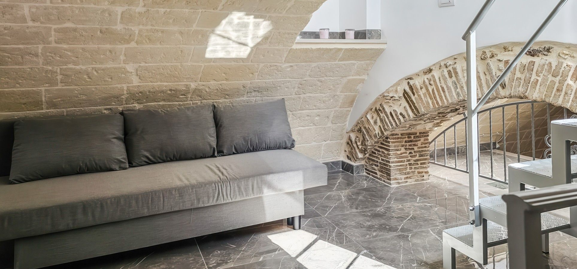 Ein modernes Interieur mit einer Steinwand, einem grauen Sofa und einer Treppe mit Ziegeloptik.