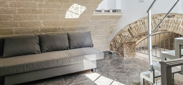 A modern interior with a stone wall, a grey sofa, and a staircase with a brick design.
