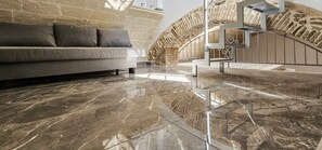 A modern living room with a marble floor, a grey sofa, and a stone wall.