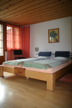 Ein Zimmer mit einem hölzernen Bett, einem Sessel, einem Fenster mit Vorhängen und einem Bild an der Wand.