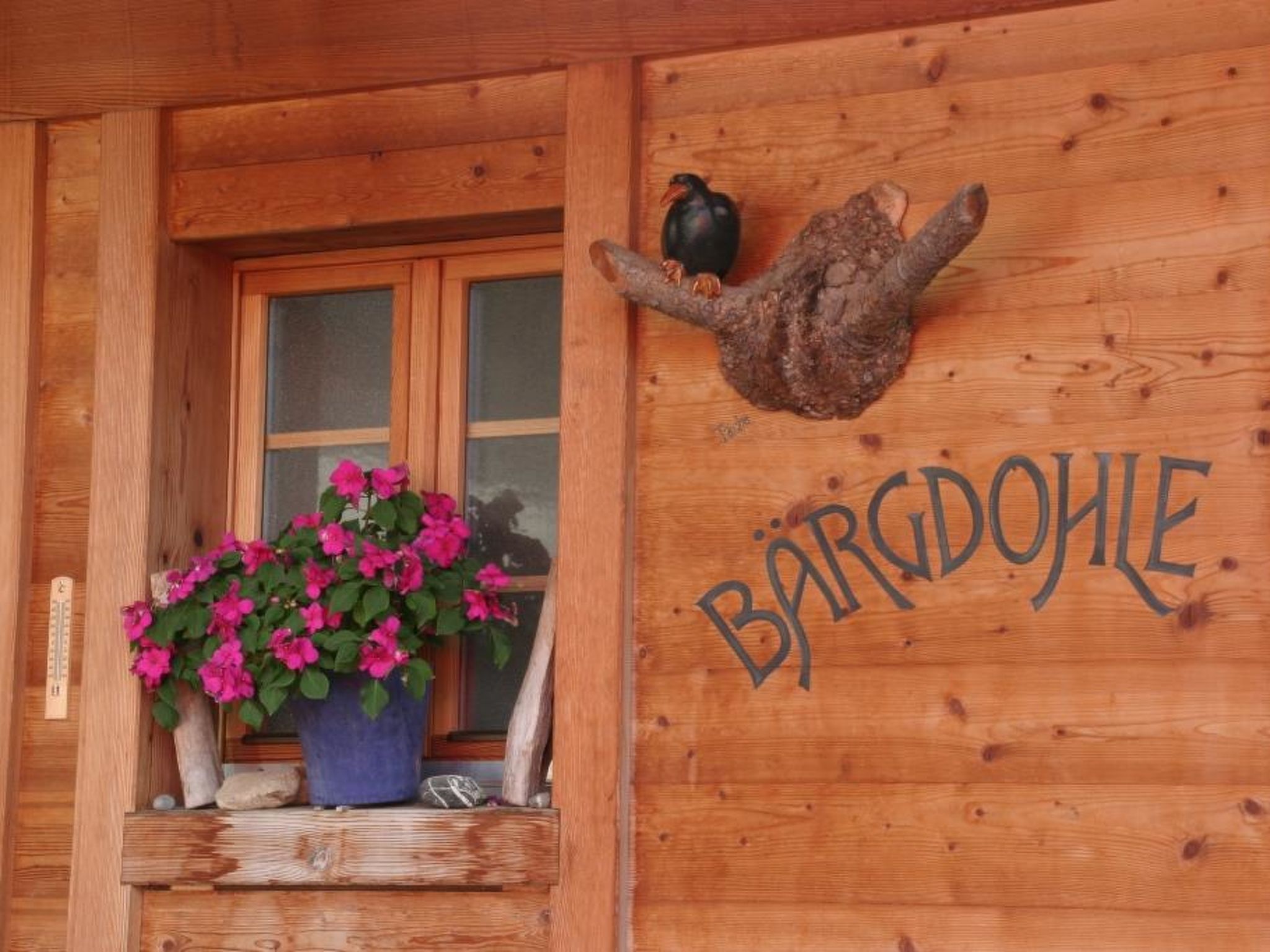 Eine Holzhütte mit einem Fenster, das pinkfarbene Blumen und ein Vogelhaus zeigt.