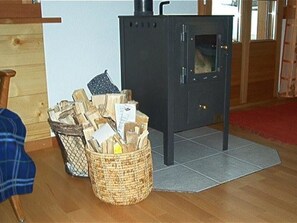 Ein Zimmer mit einem schwarzen Kaminofen, einem Korb voller Holz und einem Holzstuhl.