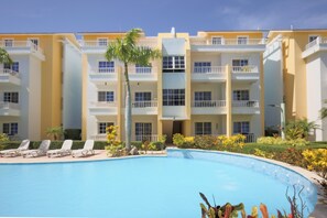 A hotel with a swimming pool, multiple balconies, and a well-maintained garden. - Estrella Del Mar F4_400Mbps_BBQ_Pool_Walk to Beach (Punta Cana)