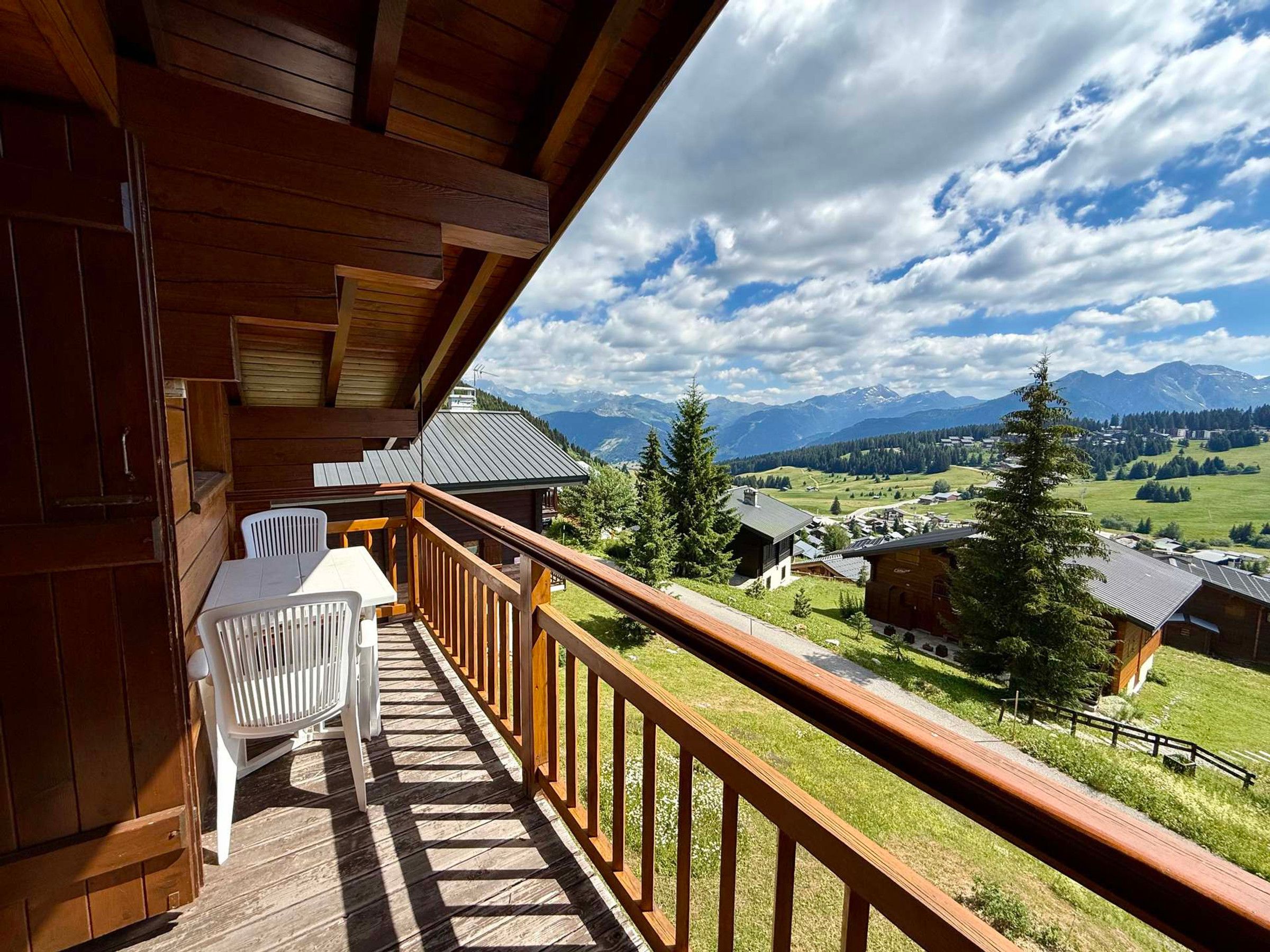 Un balcón de madera con una mesa y sillas, con vistas a un paisaje montañoso.