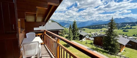 Un balcón de madera con una mesa y sillas, con vistas a un paisaje montañoso.