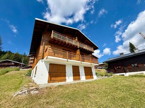 A two-story wooden chalet with a balcony, white exterior walls, and wooden shutters. - Apartment with slope view - 5 guests (Les Saisies)