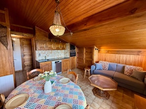 A cozy cabin interior with a wooden ceiling, a dining table set for two, a sofa, and a kitchen area. - Apartment with slope view - 5 guests (Les Saisies)