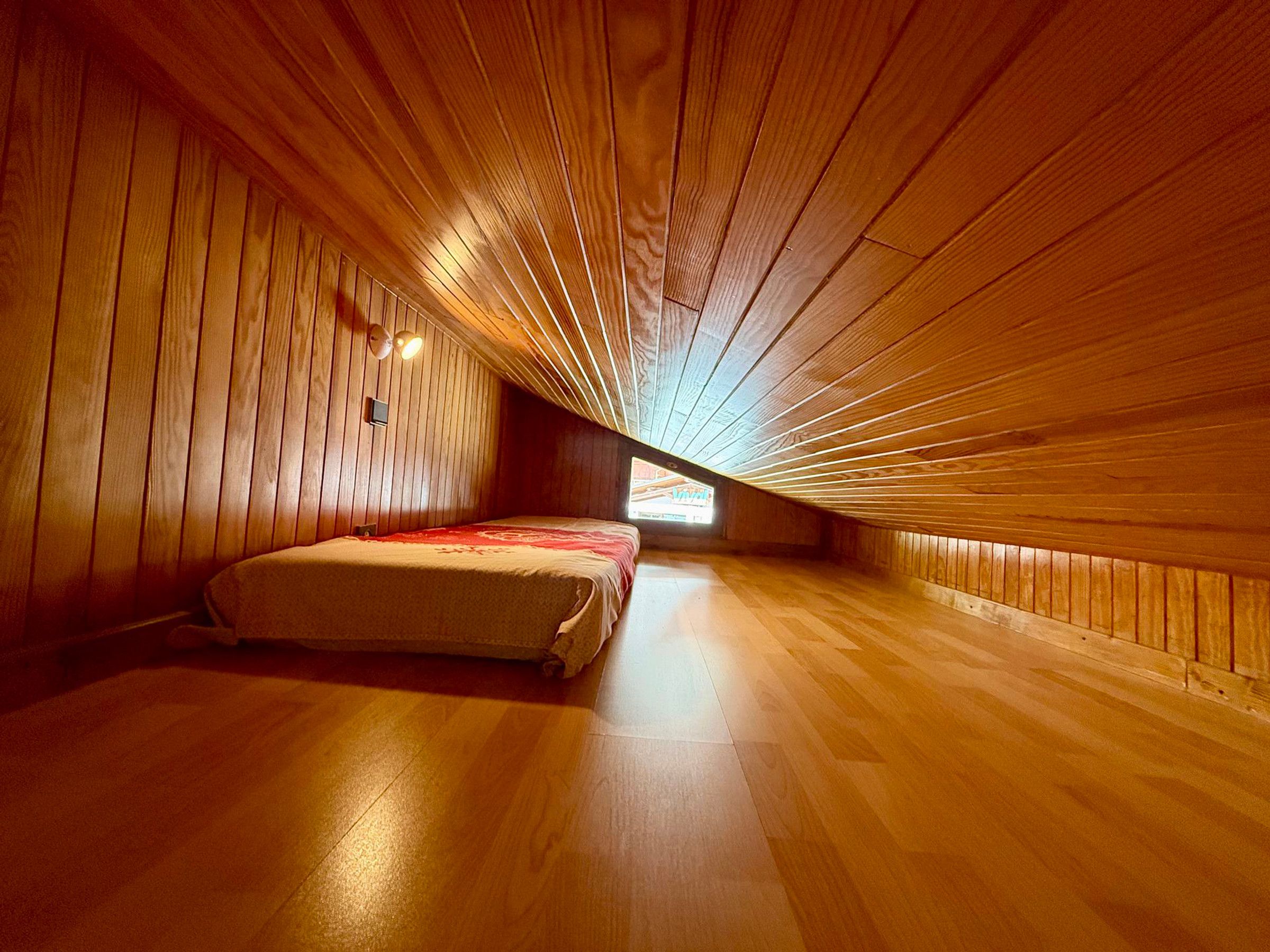 A room with wooden panel walls, a bed, and a sloped ceiling.