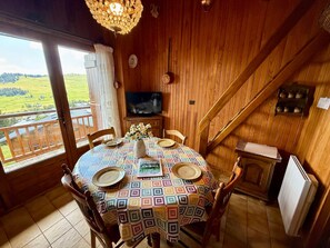 Ein Essbereich mit einem runden Tisch, Stühlen, einem Fernseher und Blick auf eine grüne Landschaft.