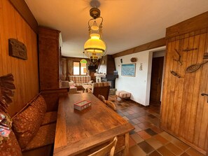 Ein gemütliches Holzambiente mit Esstisch, Stühlen und einer Bank. Im Hintergrund ist ein Kamin zu sehen, sowie Holzschränke und ein Fliesenboden.