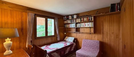 A cozy room with a bed, a desk, a chair, a bookshelf, and a window with curtains.
